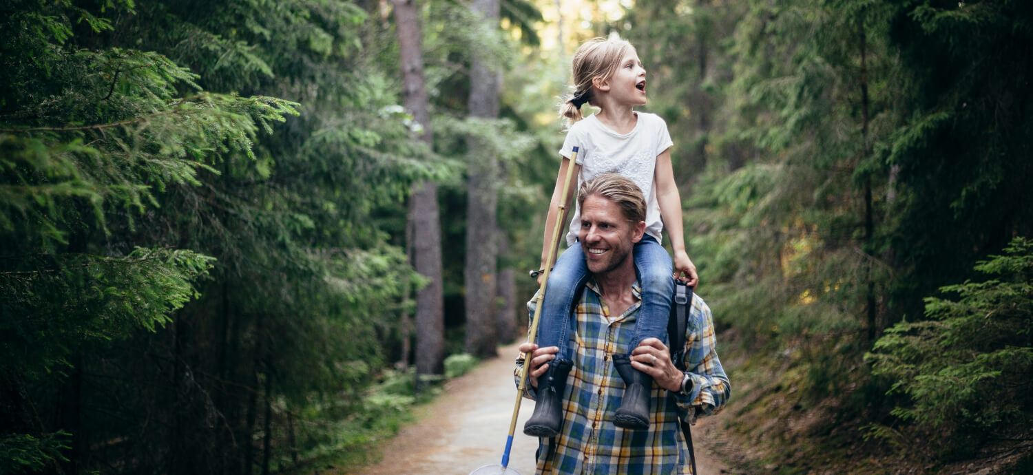 daughter on father's shoulders walking through the forest