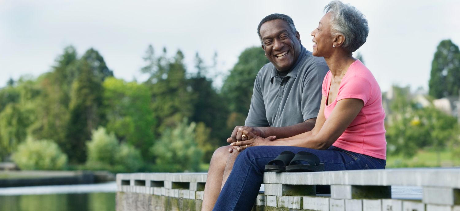 two african american senior adults sitting on a dock laughing